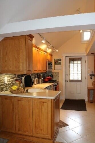 A kitchen with oak cabinets, a white countertop, stone backsplash, and a door leading to the outside.