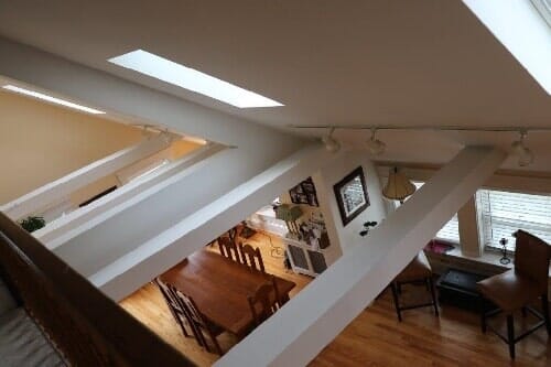 Loft-style interior with exposed beams, skylight, wooden floors, and a dining area below.