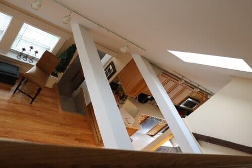 An interior view looking down from a loft onto a kitchen area with wood cabinets, hardwood floors, and a brown stool.