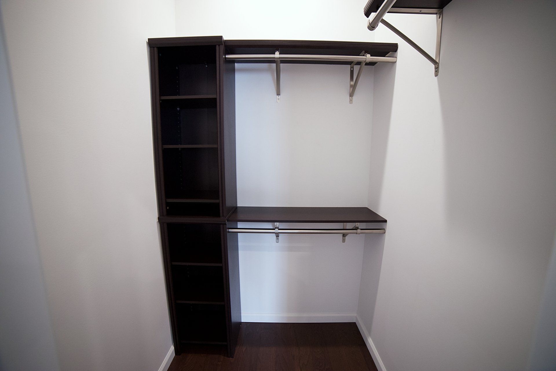A walk-in closet featuring a dark brown shelving unit with hanging rods, set against plain white walls.