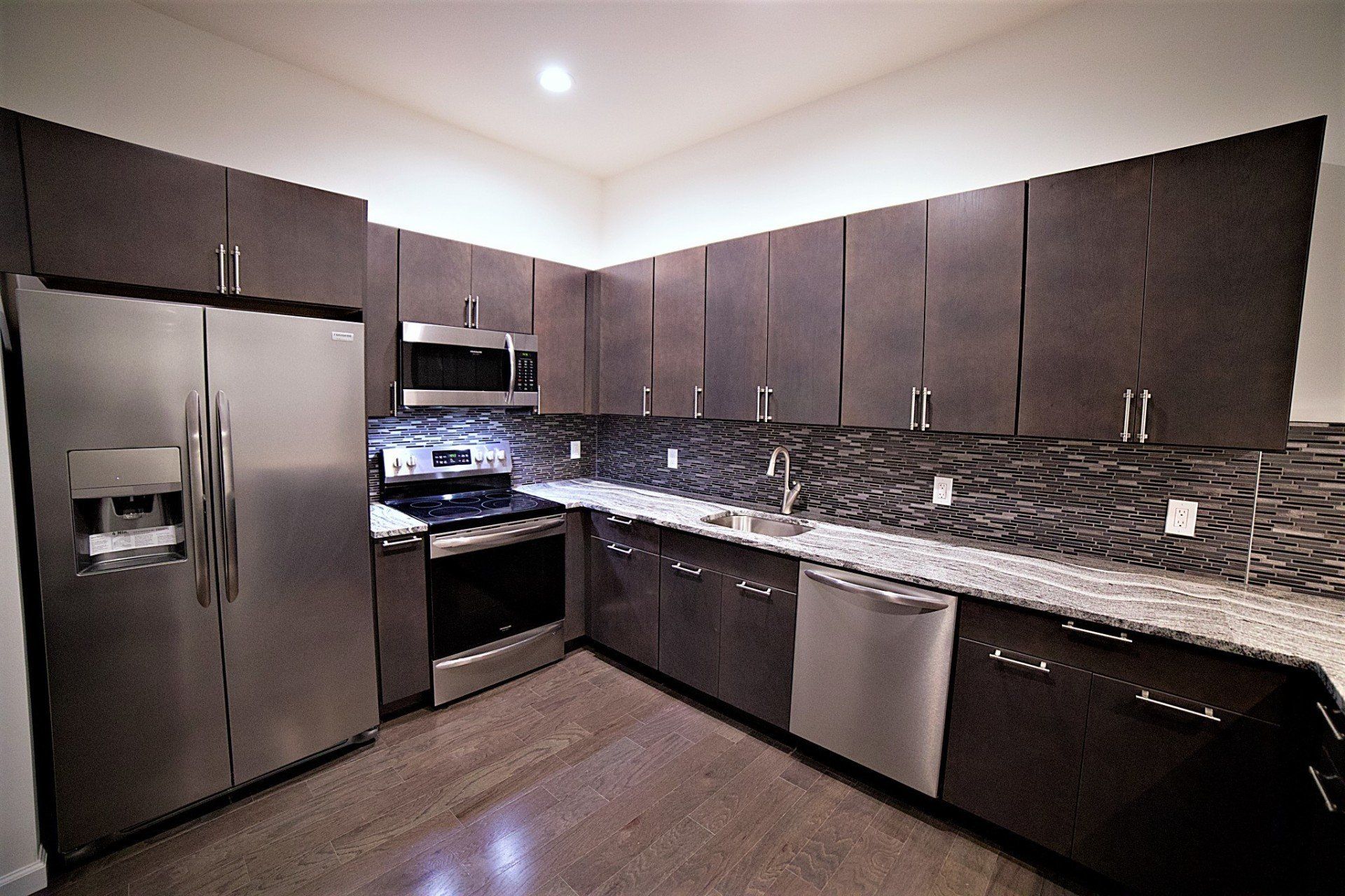 Modern kitchen with dark wood cabinets, stainless steel appliances, granite countertops, and a patterned backsplash.