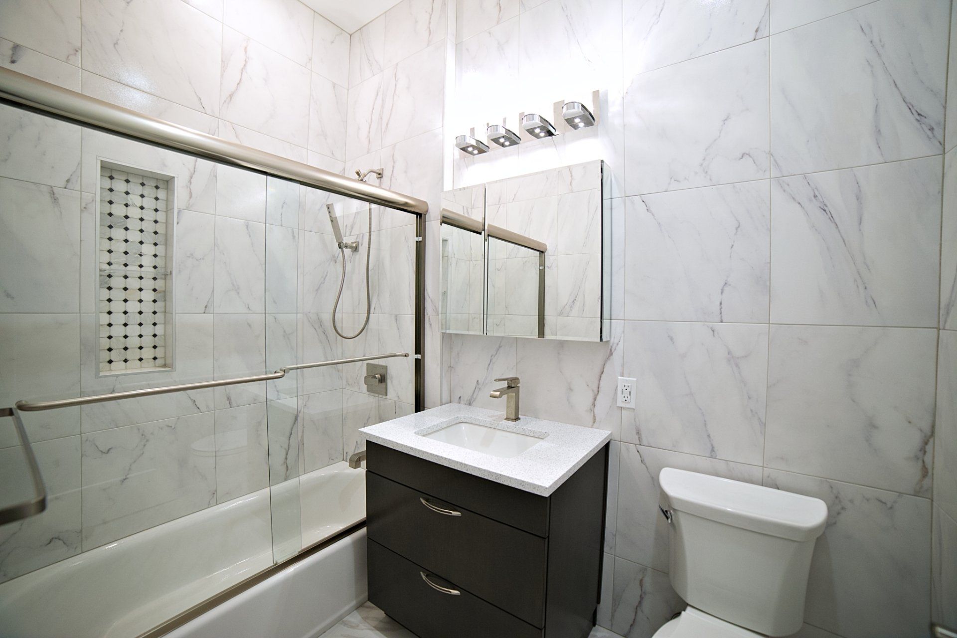 Modern bathroom with marble-tiled walls, glass-enclosed shower, dark wood vanity, and white toilet.