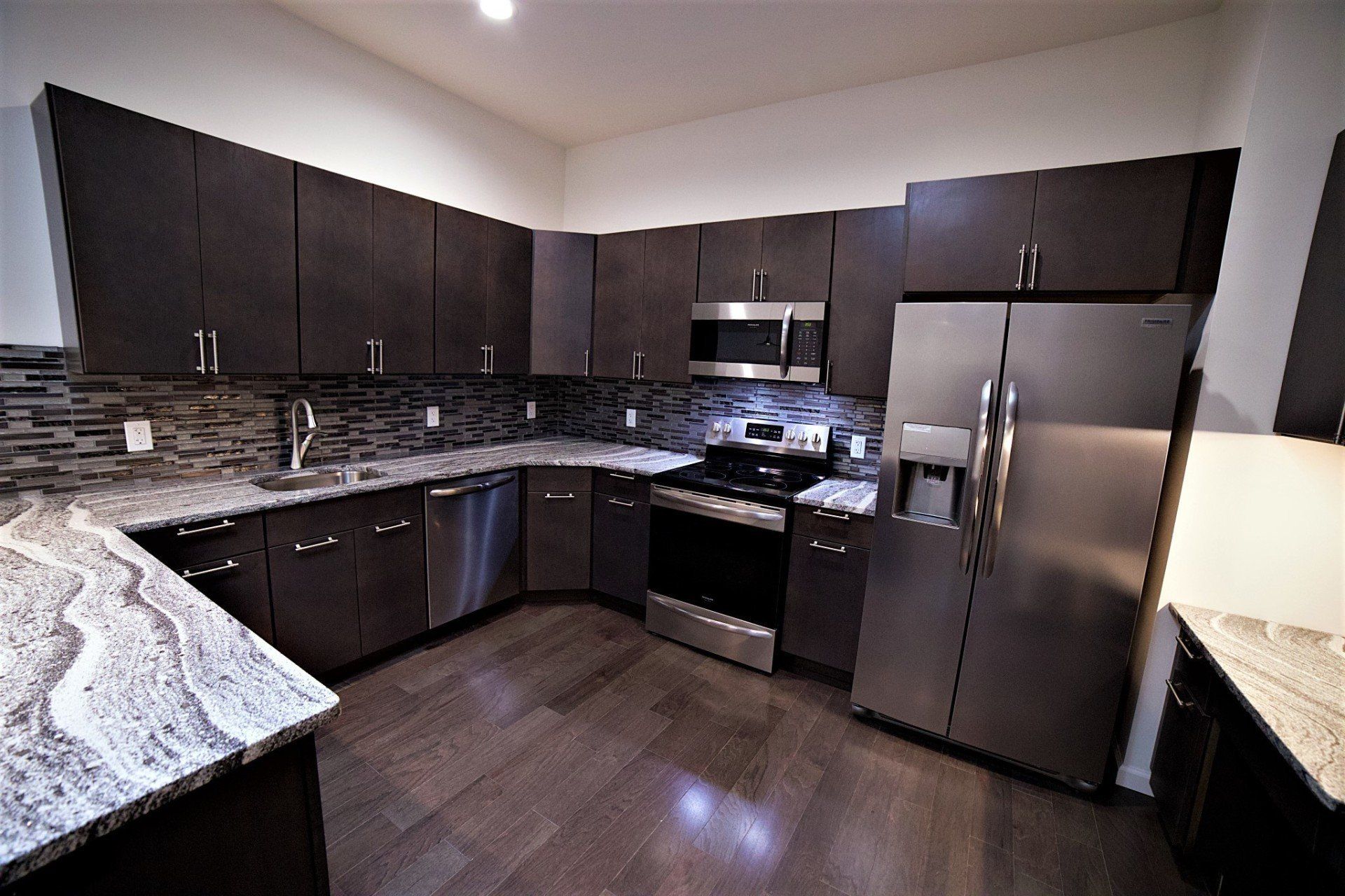 Modern kitchen with dark cabinets, stainless steel appliances, granite countertops, and wood-look flooring.