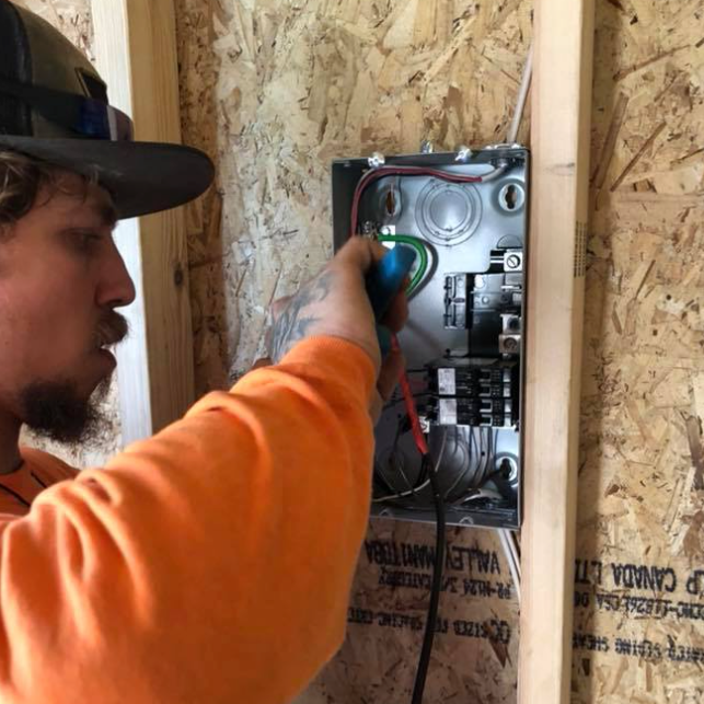 A man wearing a hat is working on an electrical box.
