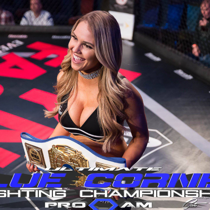 A woman in a bikini is holding a championship belt in a boxing ring