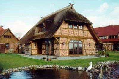 Ein Haus mit Strohdach und einem Teich davor.