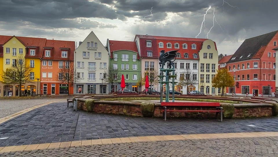 pixabay, lizenzfrei In der Mitte eines Stadtplatzes steht ein Brunnen, im Hintergrund ist ein Blitz zu sehen.