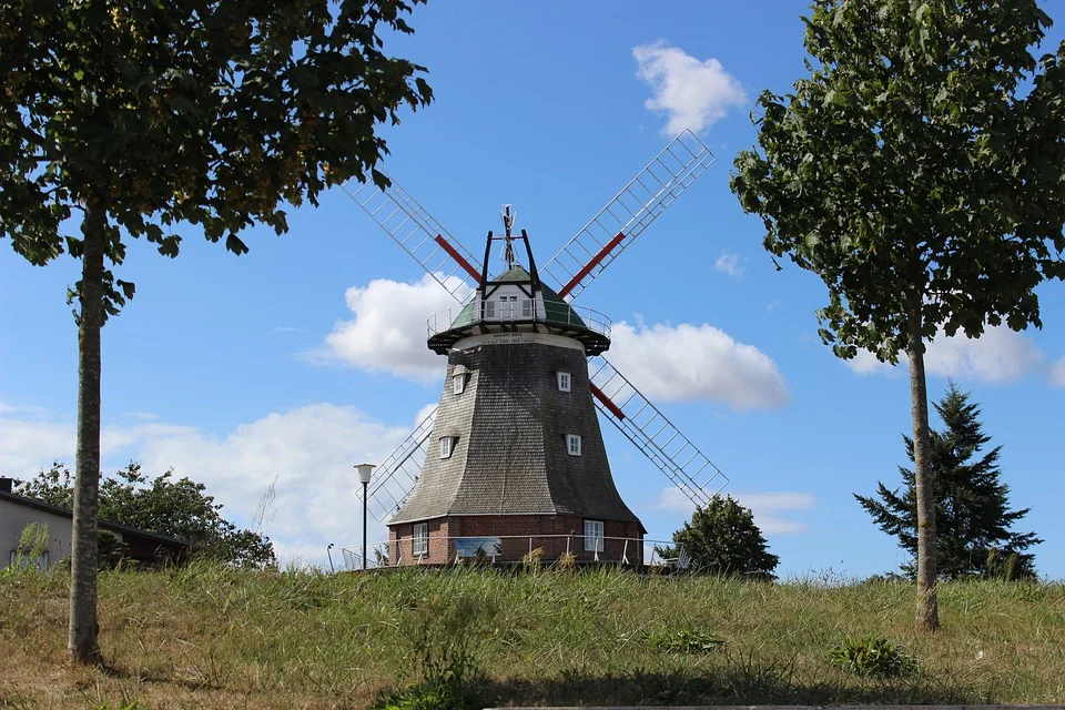 pixabay, lizenzfrei Eine große Windmühle steht auf einem grasbewachsenen Hügel, umgeben von Bäumen.