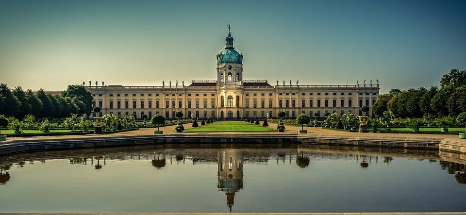 pixabay, lizenzfrei Ein großes Gebäude mit einem Uhrenturm spiegelt sich in einem Teich.