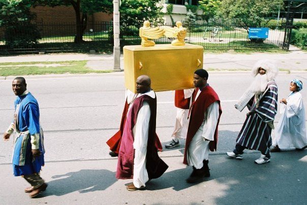 A group of people are walking down a street carrying a large gold box