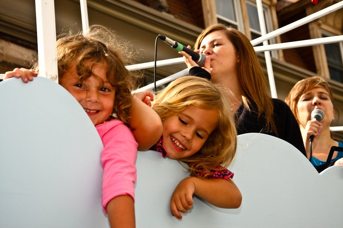 A woman is singing into a microphone while two little girls look on
