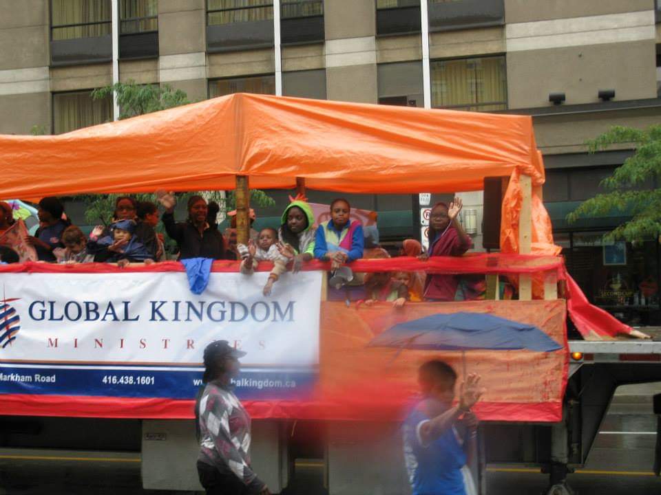 A group of people are riding on the back of a truck that says global kingdom
