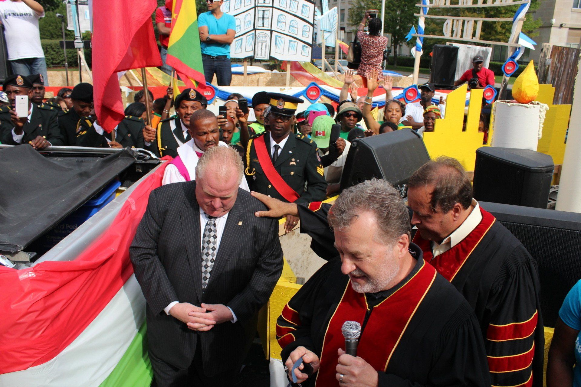 A group of men are standing in front of a flag and one man is holding a microphone