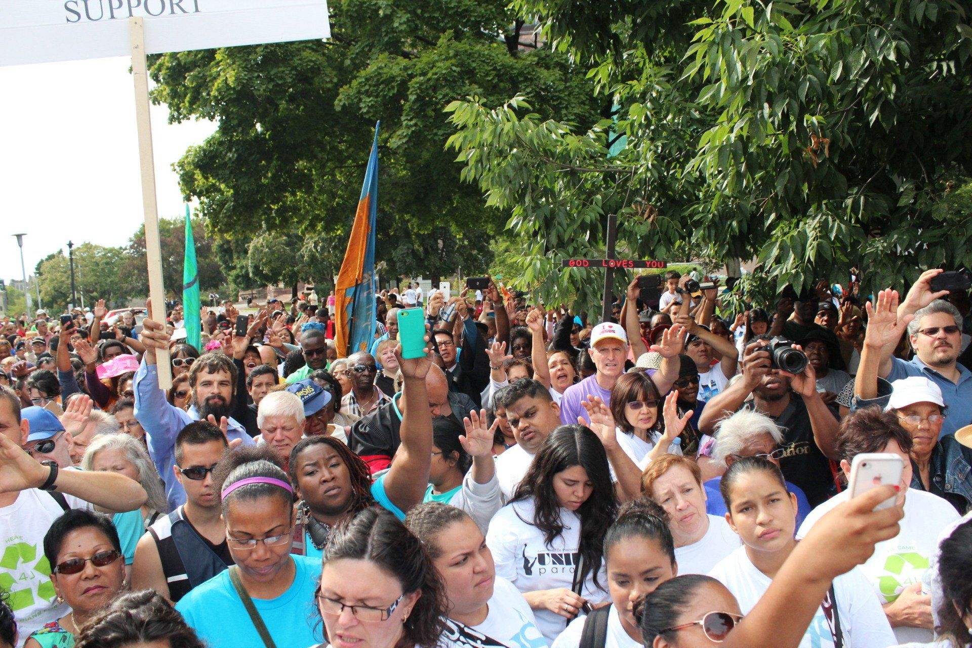 A crowd of people are gathered in a park with a sign that says support