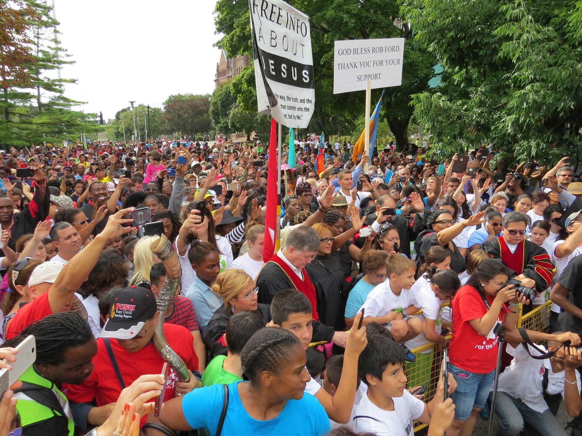 A large crowd of people are gathered in a park holding signs.