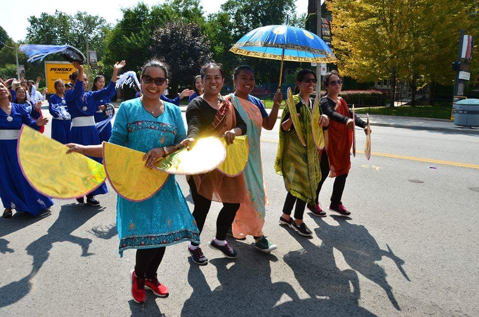 A group of women are walking down a street holding umbrellas and fans
