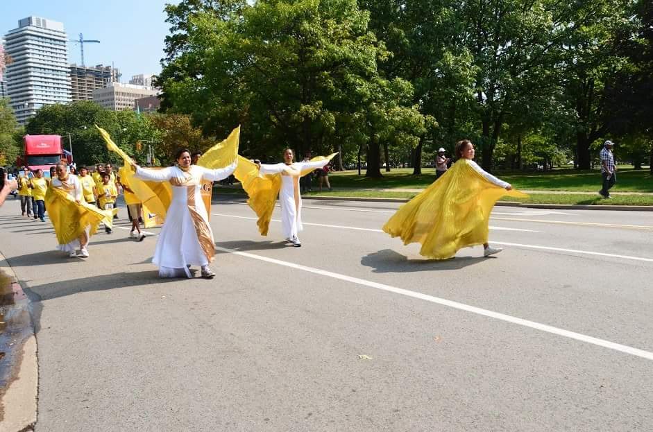 A group of people in yellow dresses are walking down a street
