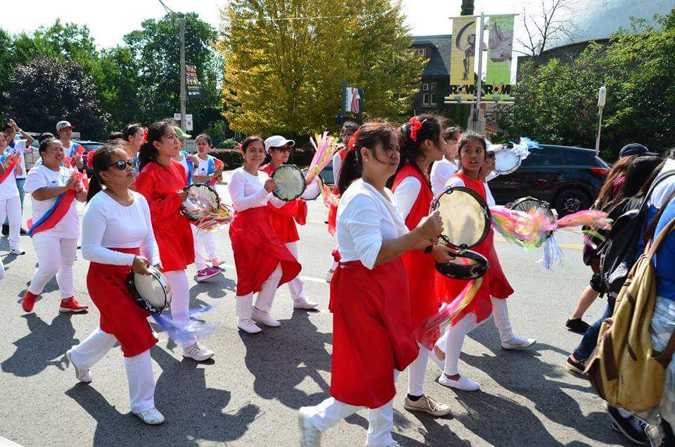 A group of young girls are marching down a street holding tambourine.