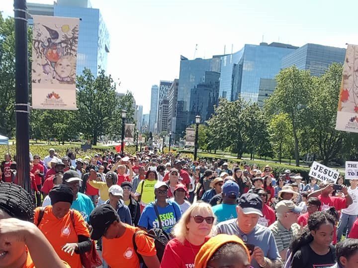 A crowd of people marching down a street with a sign that says jesus