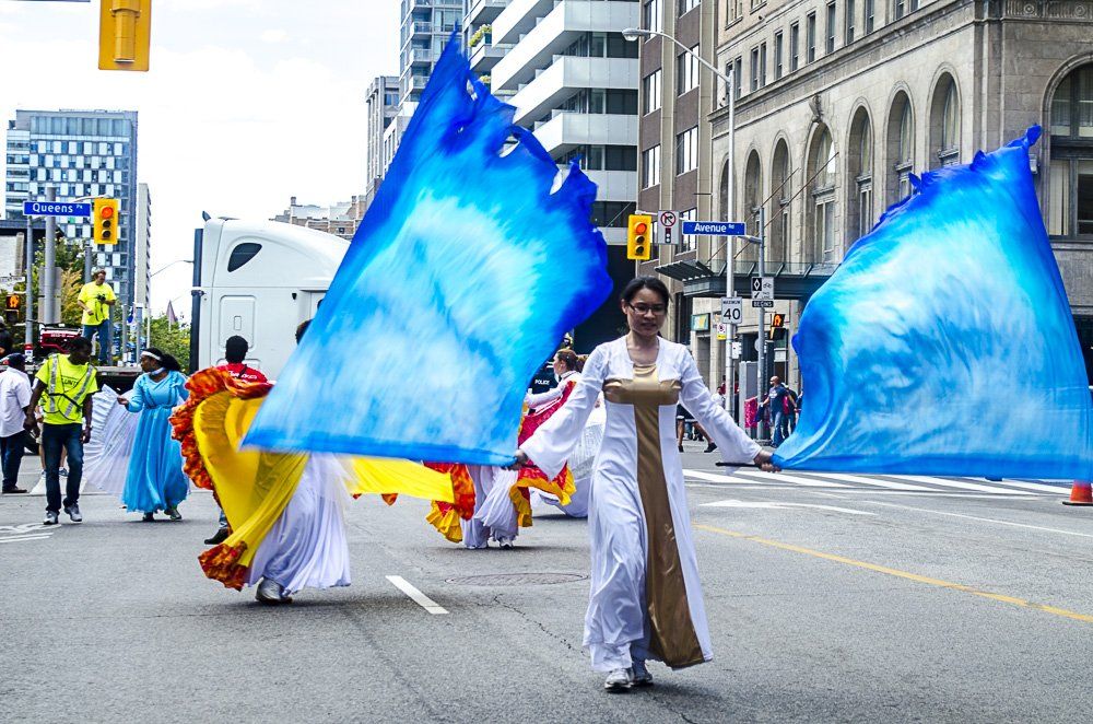 A woman in a white dress is holding a blue flag in a parade.