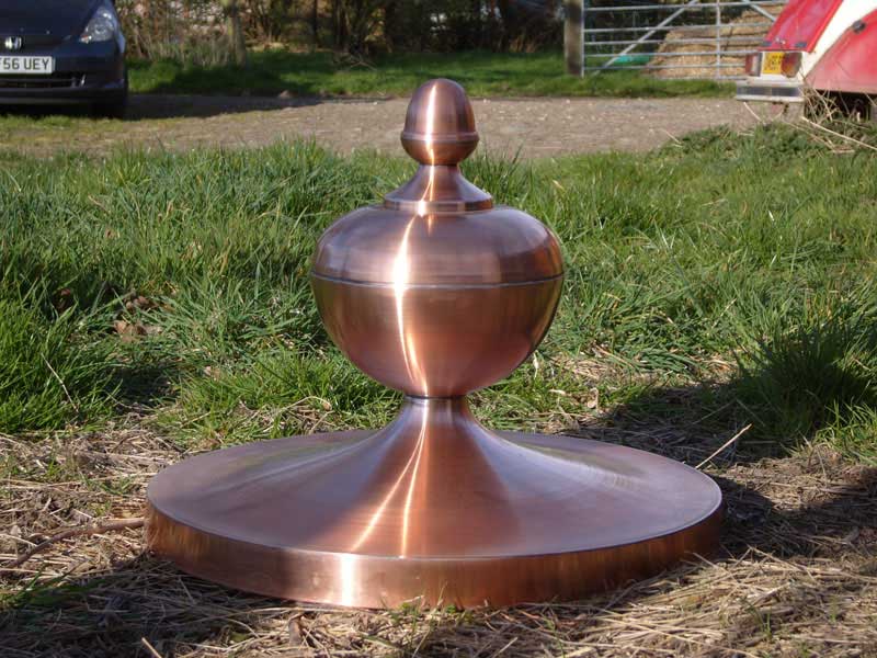 A copper object is sitting in the grass in front of a car