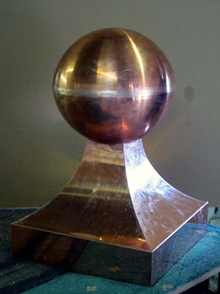 A copper ball is sitting on top of a metal base on a table.
