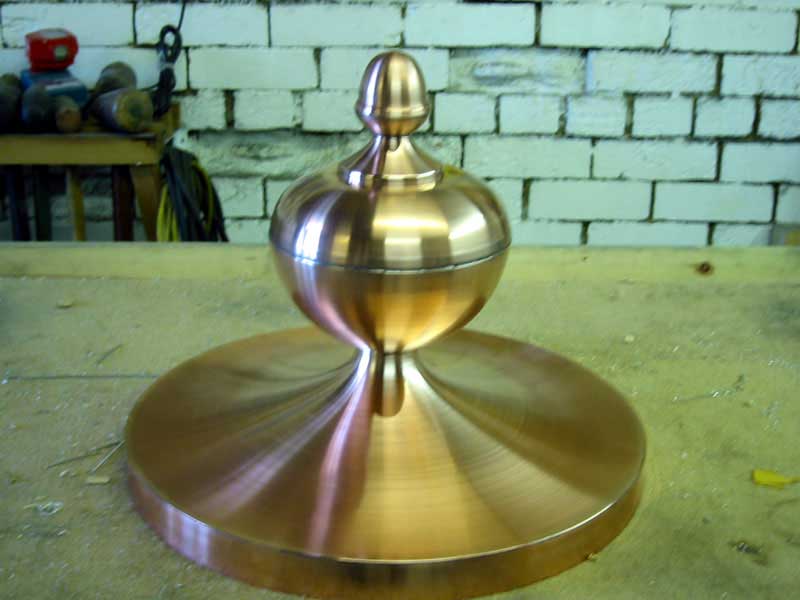 A copper object is sitting on a table in front of a brick wall
