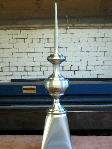 A metal object with a pointed top is sitting in front of a brick wall