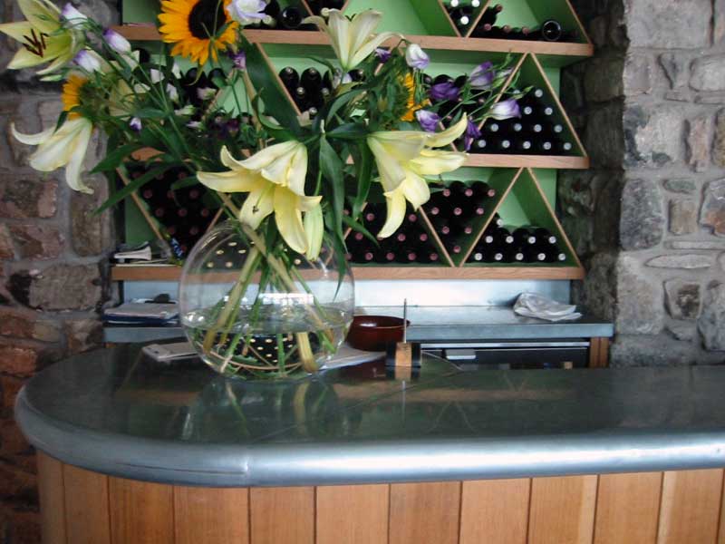 A vase of flowers sits on a counter in front of a wine shelf
