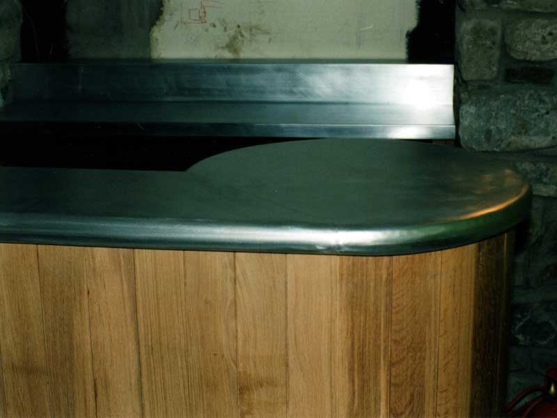 A wooden counter with a metal top is sitting next to a stone wall.