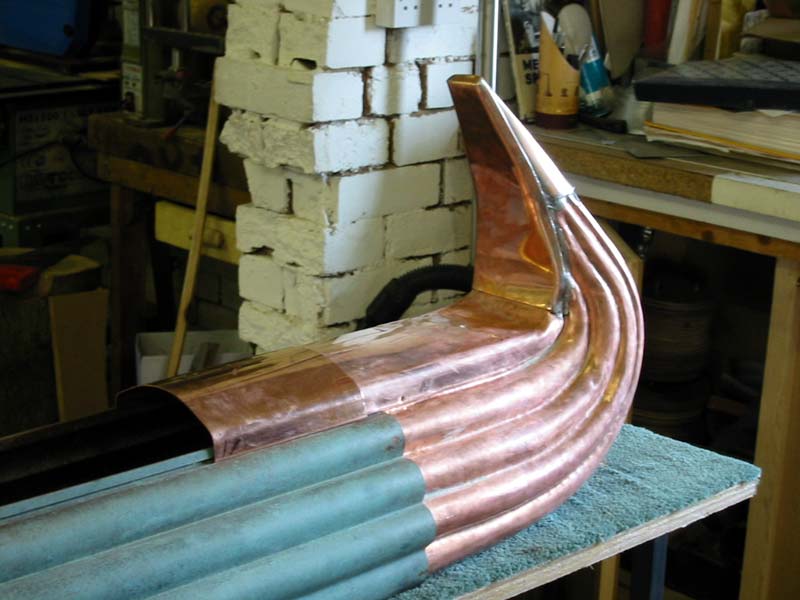 A copper pipe is sitting on a table in front of a brick wall