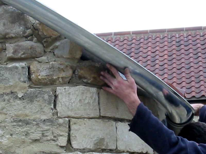 A person is holding a metal pipe against a stone wall