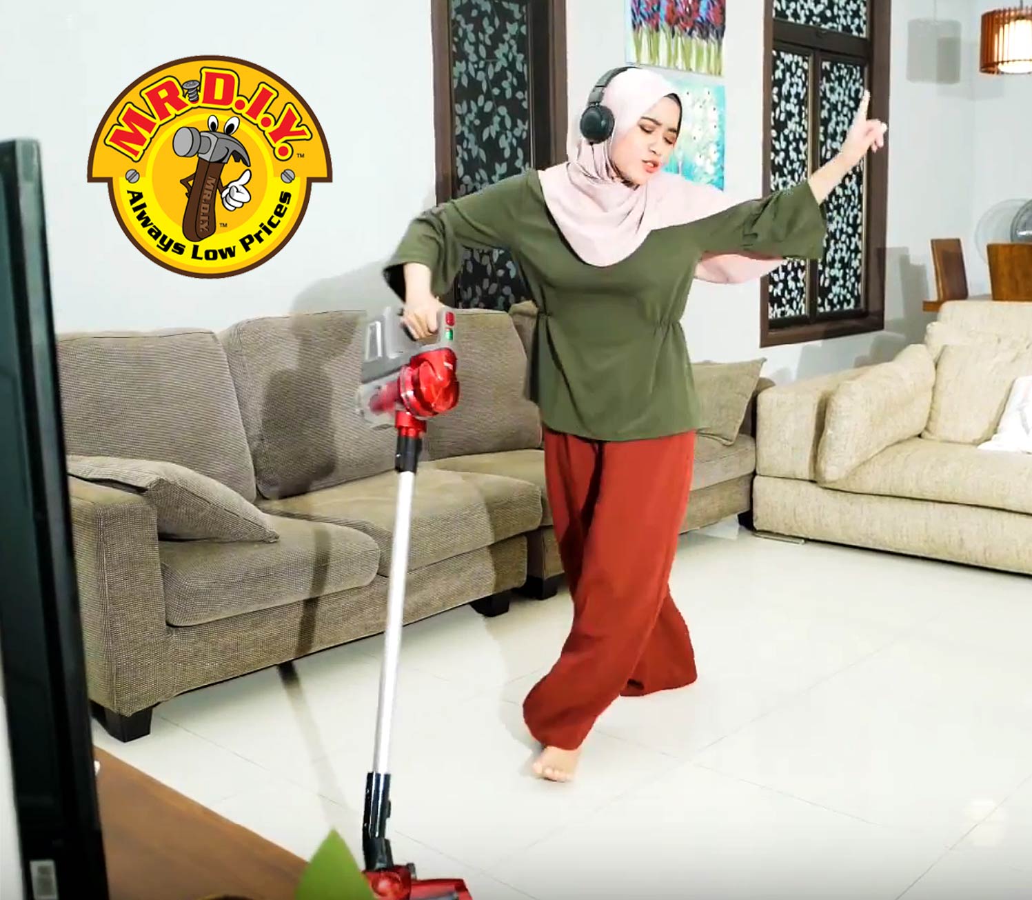 Woman posing beside a vacuum cleaner in a bright living room with sofas and a patterned window.