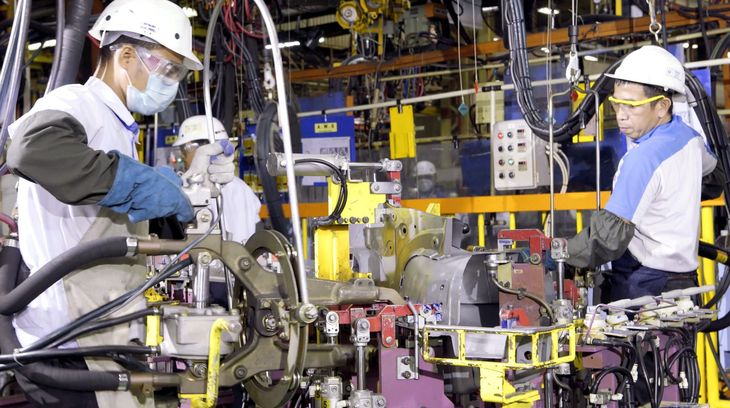 Two workers in white hard hats inspect machinery on an industrial assembly line.