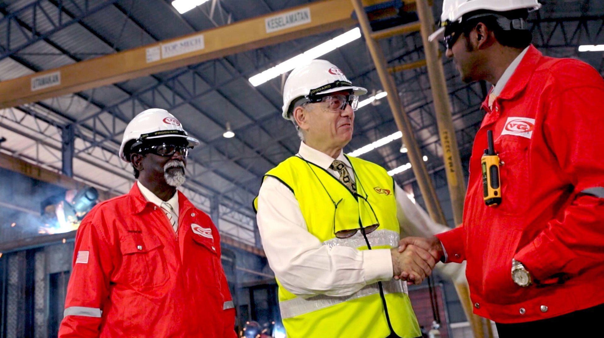 Three workers in safety gear shaking hands inside an industrial warehouse