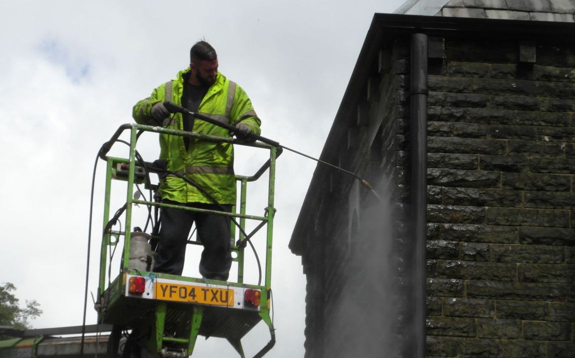 A man is cleaning the side of a building with a high pressure washer.