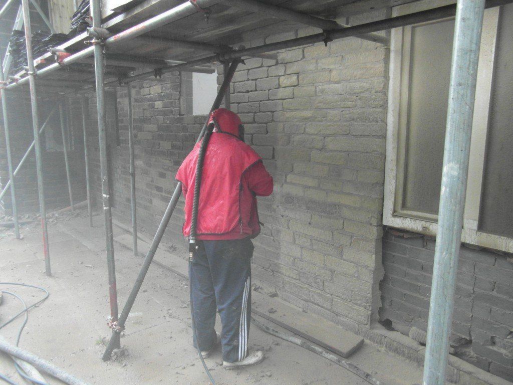 A man in a red jacket is standing next to a brick wall.
