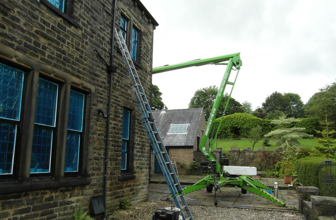 A green crane is sitting in front of a brick building.