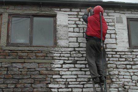 A man is standing on a ladder cleaning a brick wall.
