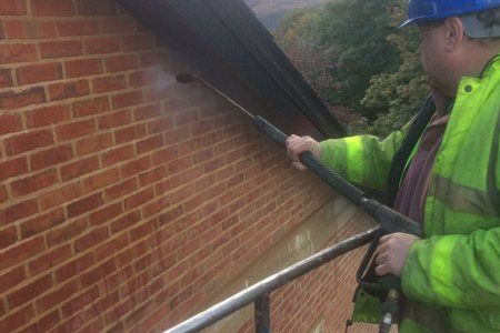 A man is cleaning a brick wall with a high pressure washer.