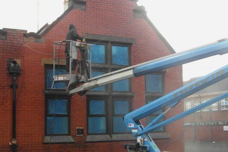 A man is cleaning a brick building with a crane.