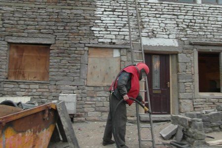 A man is standing on a ladder in front of a brick building.