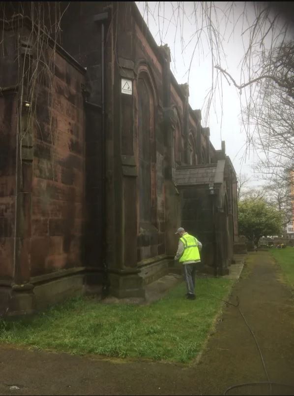 A man in a yellow vest is standing in front of a building.