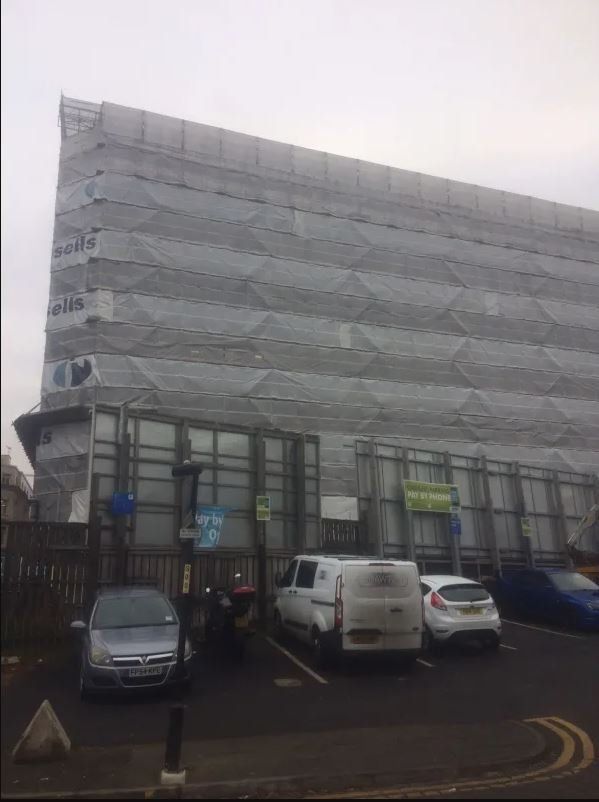 A large building is covered in scaffolding and cars are parked in front of it.