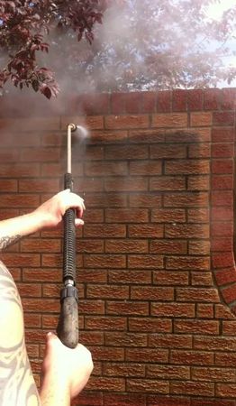 A person is cleaning a brick wall with a high pressure washer.