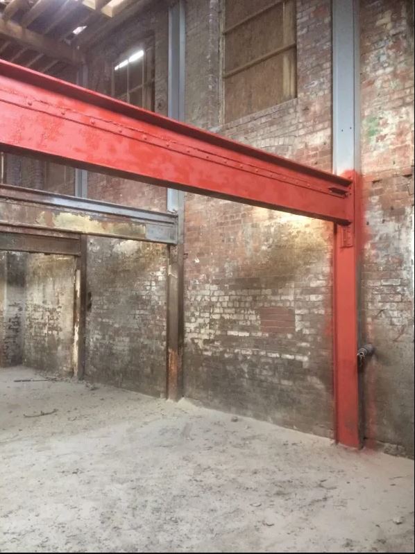 An empty room with a red beam between two brick walls