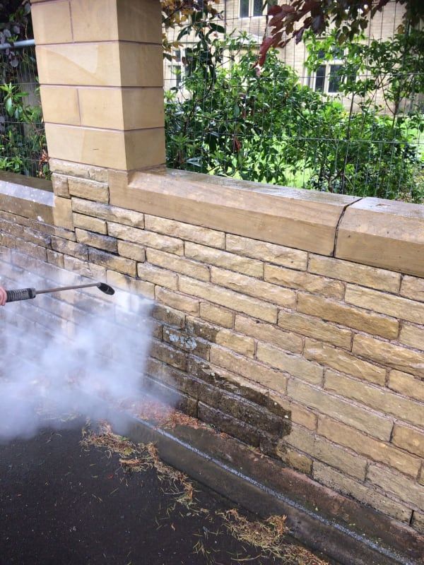 A person is cleaning a brick wall with a high pressure washer.