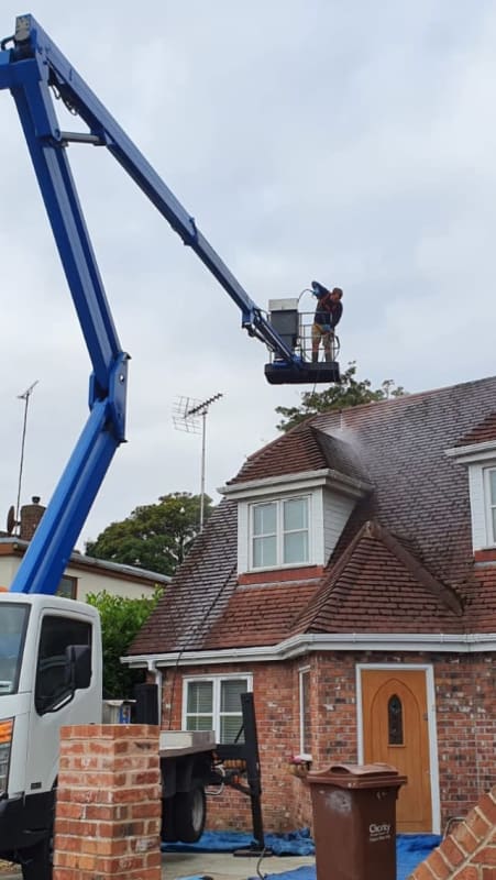 A man is cleaning the roof of a house with a crane.