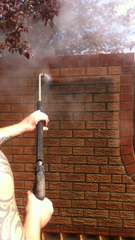 A man is cleaning a brick wall with a high pressure washer.