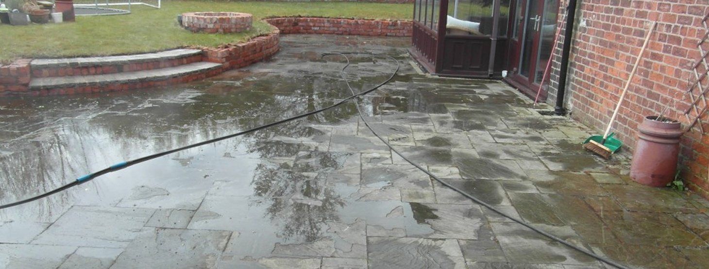 A patio with a hose attached to it and a brick building in the background.